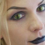 Close-up portrait of young pretty woman with halloween makeup at beauty salon. Face of lady with cat eyes contact lenses.