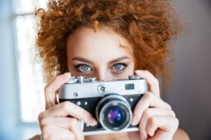 Attractive redhead curly young woman photographer using old camera